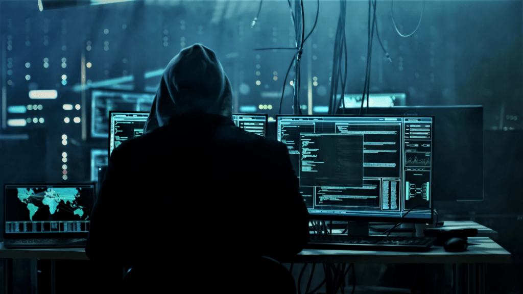 a person in a hoodie sitting at a desk with multiple monitors