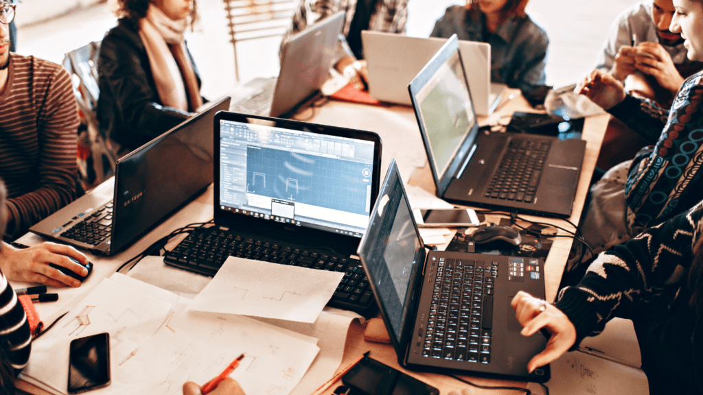 a group of people sitting around a table with laptops