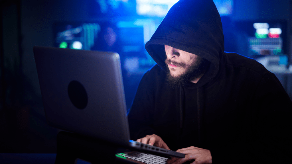 a person in a hoodie sitting at a desk with multiple monitors